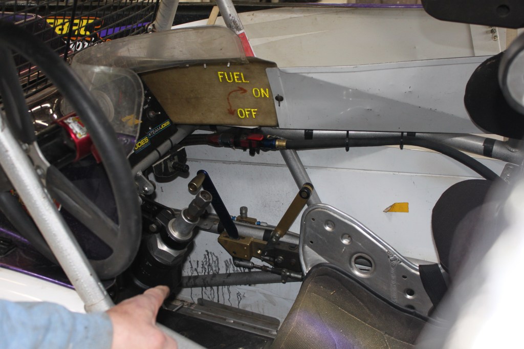 Interior view of a modified dirt racing car, showcasing the steering wheel, control panel with 'FUEL ON/OFF' sign, and racing seat.